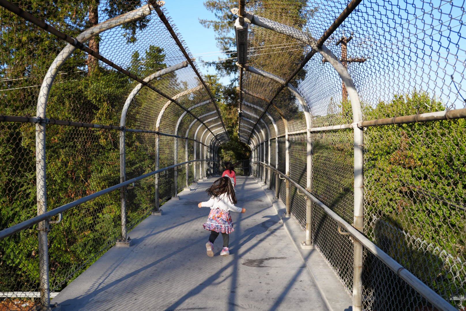 Child running away down a fenced pedestrian bridge at golden hour